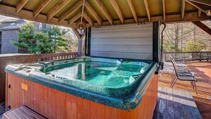 Un jacuzzi bajo una pérgola de madera, con vistas a casas y árboles.