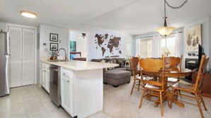 Cocina compacta con una isla central, zona de comedor con sillas de madera y un mapa mundial en la pared.