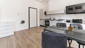 A modern kitchen with white cabinets, a flat-screen TV, and a dining area with a glass table and chairs. - Vatican Suites Apartment - Vatican City (Rome)