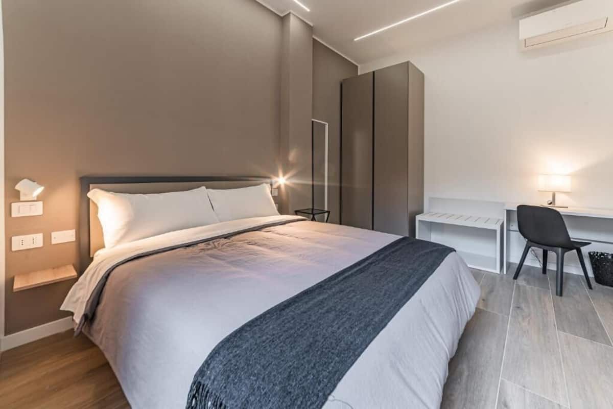 A modern bedroom with a bed, bedside table, desk, chair, and wardrobe.
