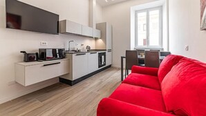 A modern kitchen with a flat-screen TV, a dining area with a red sofa, and a large window. - Vatican Suites Apartment - Vatican City (Rome)
