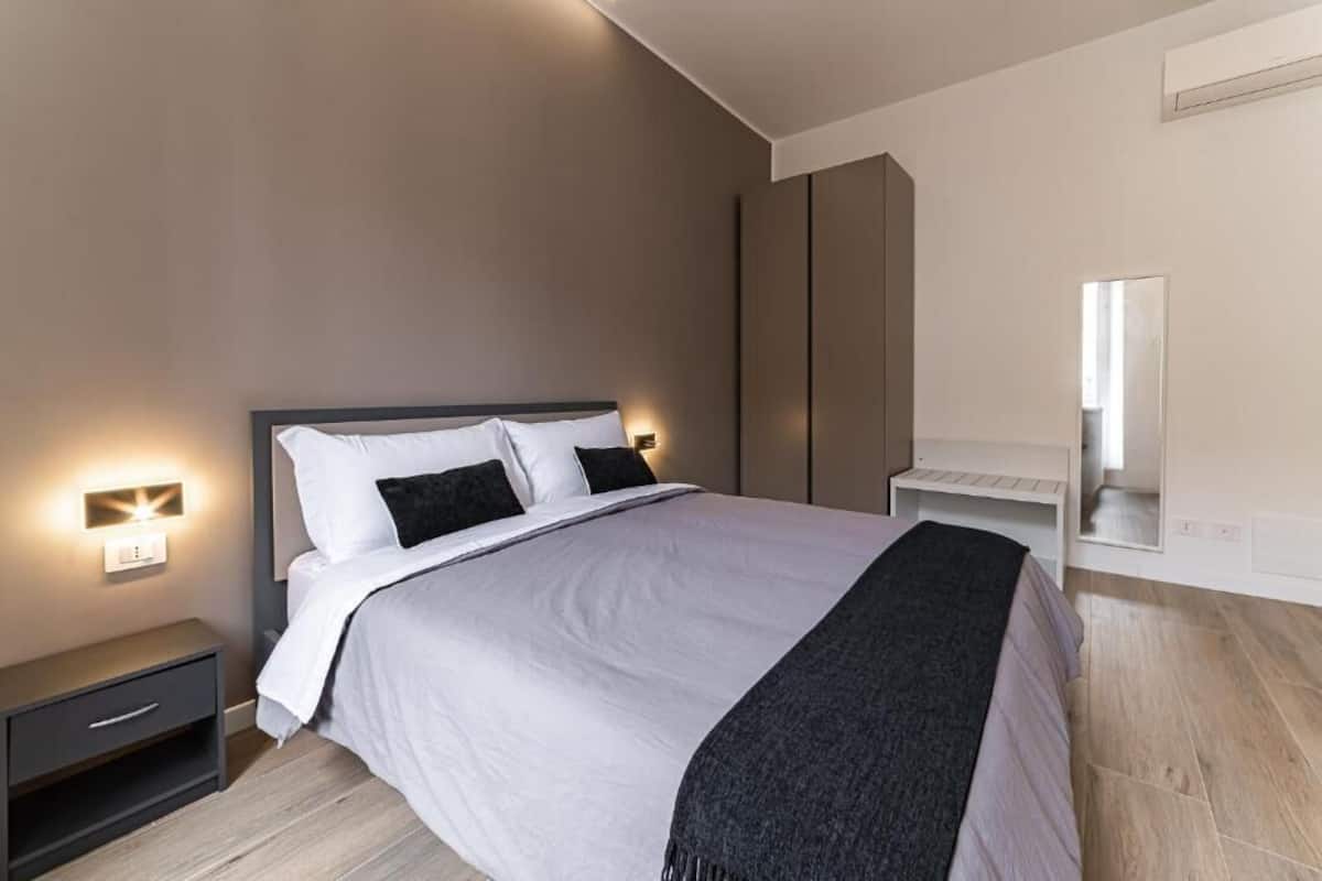 A modern bedroom with a bed, bedside tables, a nightstand, a mirror, and built-in wardrobes.