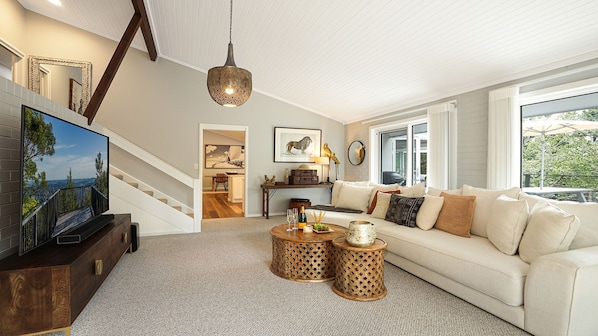A spacious living room with a large flat-screen TV, a staircase, a sofa set, and a dining area. - Arcadia Cottage - spacious, stylish Highlands stay for families and groups near Bowral (Bowral)