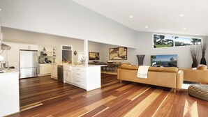 Een ruime woonkamer met een grote bank, een eettafel en een keuken met witte kasten en een roestvrijstalen koelkast.