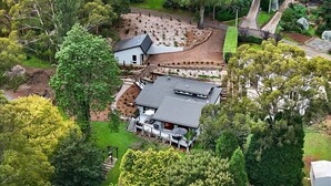 Luchtbeeld van een modern huis met een schuin dak, omringd door een verzorgde tuin en bomen.