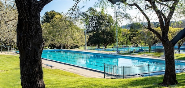 A rectangular swimming pool with a metal fence, surrounded by grass and trees.