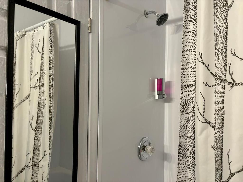 A bathroom with a shower, a mirror, and a curtain with a tree pattern.