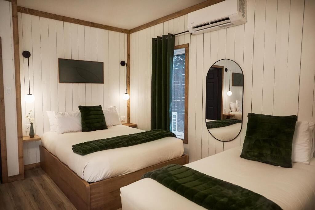 A room with two beds, a mounted TV, a mirror, and an air conditioning unit.