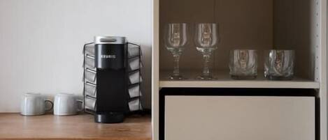 Una kitchenette con cafetera, microondas y copas de vino en un estante.