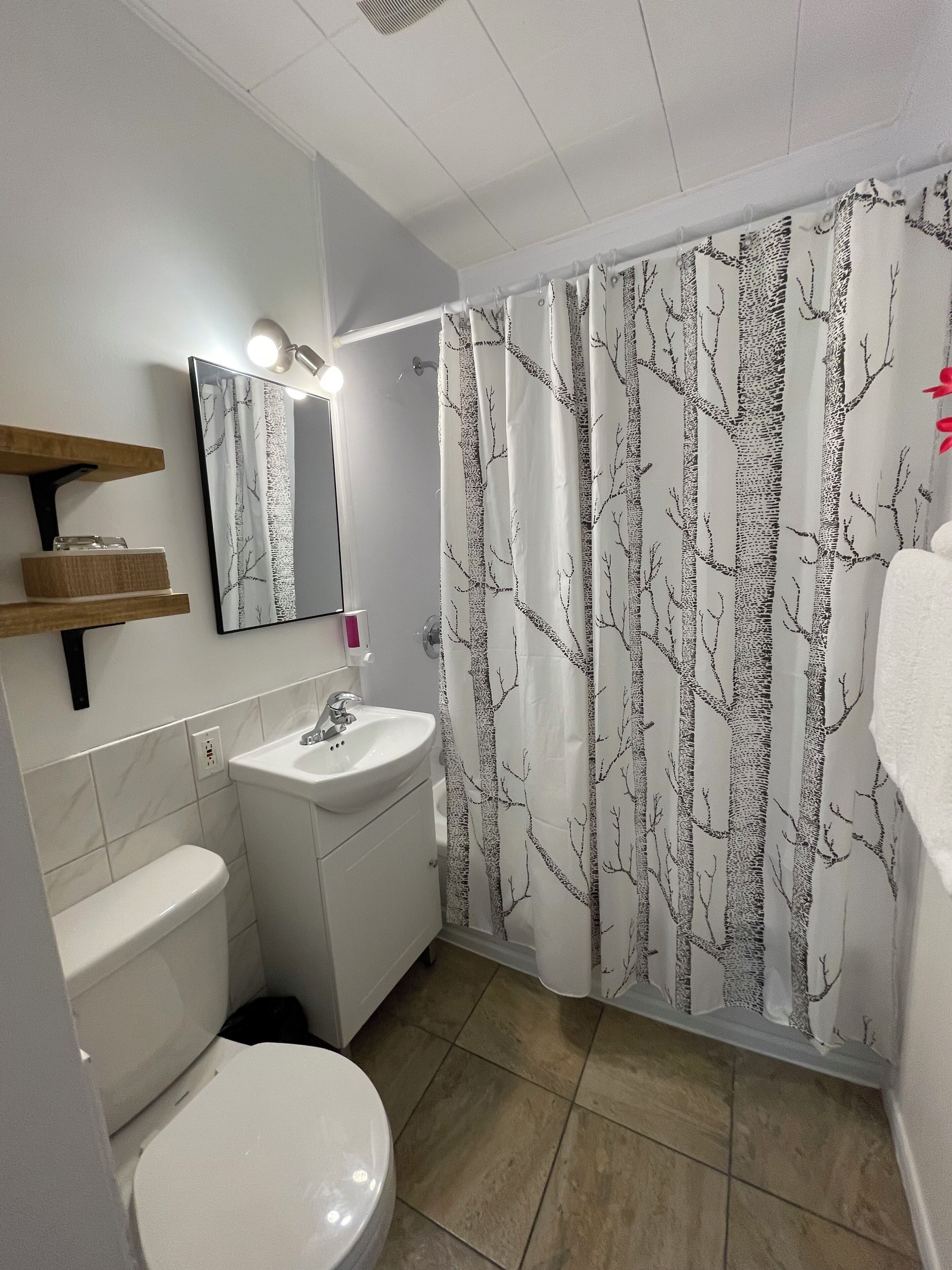 Ein Badezimmer mit Toilette, Waschbecken, Spiegel und Duschvorhang mit Baummuster.