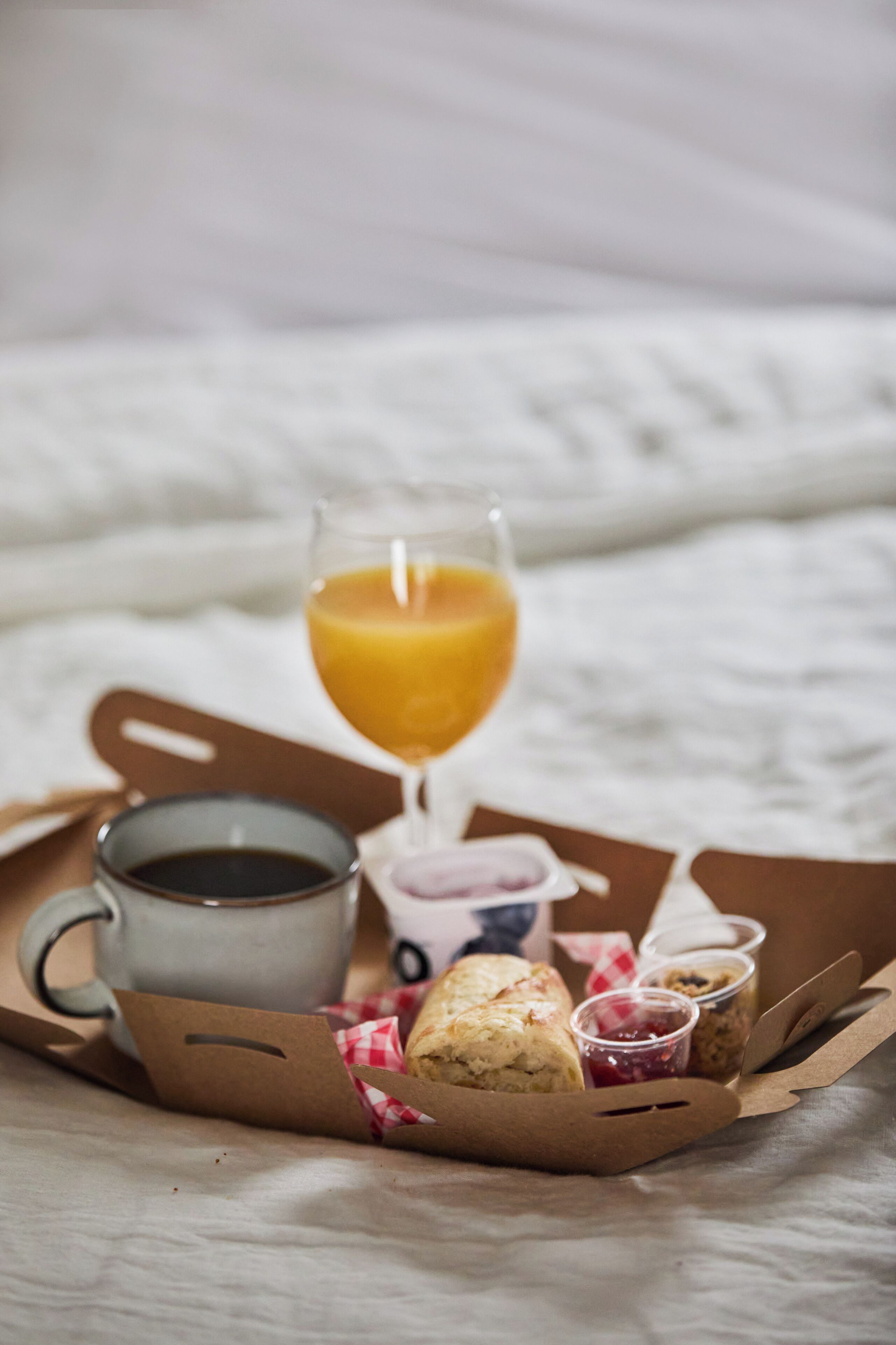 A breakfast tray with a glass of orange juice, a cup of coffee, a pastry, and small containers of jam and cream.