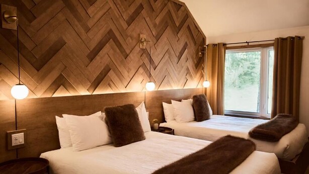Une chambre d’hôtel avec deux lits, des lambris en bois et une fenêtre avec des rideaux.