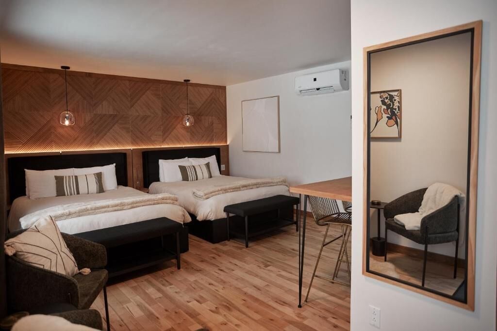 A modern hotel room with two beds, a desk, a chair, and a large mirror.