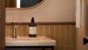 Une salle de bain avec un miroir rond, un lavabo et un flacon de savon pour les mains.