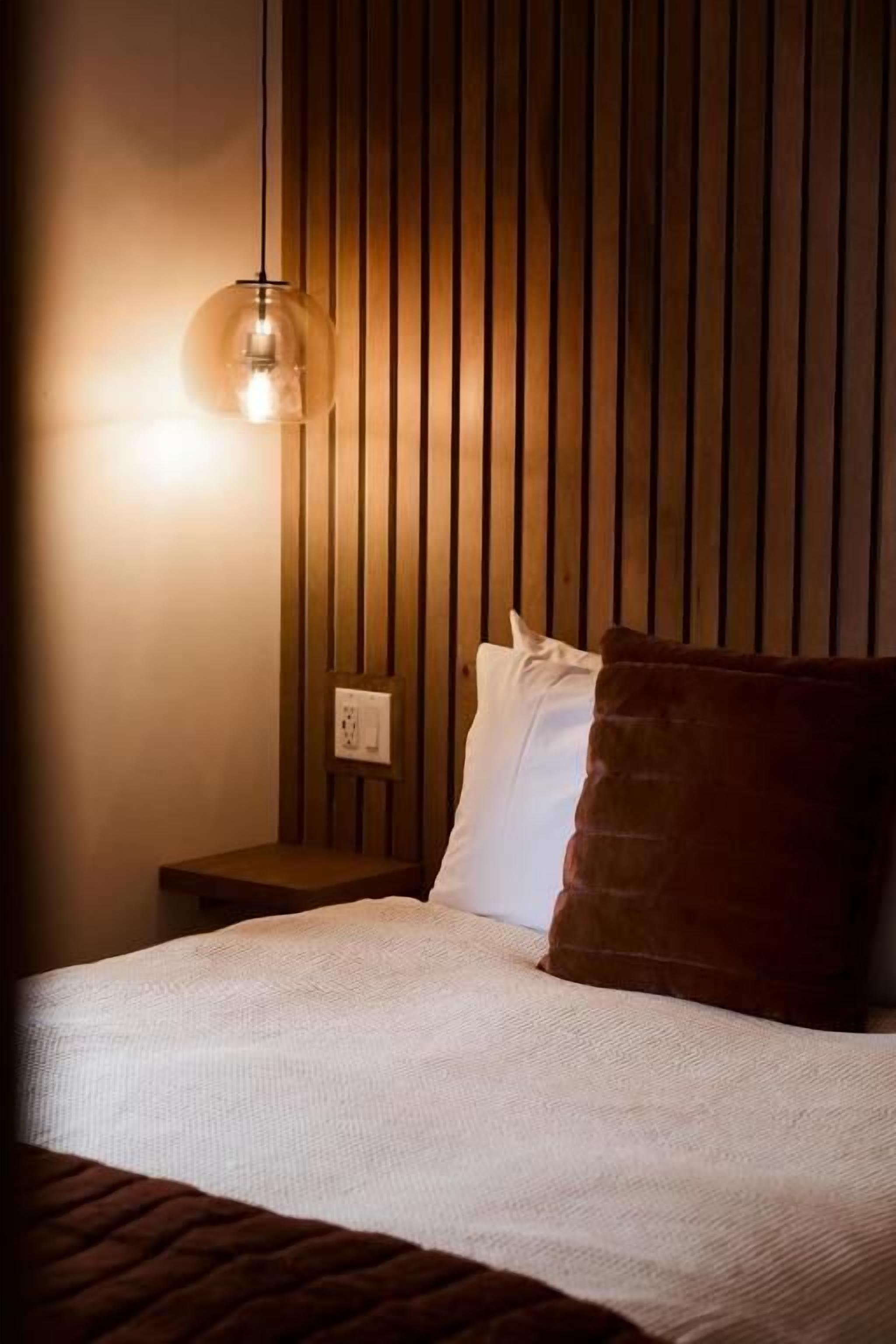 A bedroom with a bed, pillows, a nightstand, and a wall-mounted lamp.