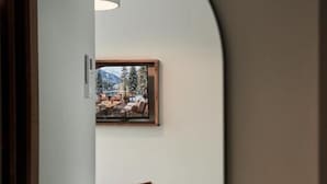 Una stanza con pavimento in legno, un divano nero con un cuscino marrone e un tappeto bianco e morbido, con un quadro appeso al muro.