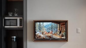 Una cucina con forno a microonde, macchina del caffè e frigorifero. È presente una barra in legno con due sedie in metallo e un quadro appeso al muro.