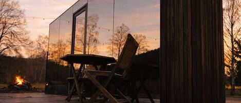 A modern wooden structure with a reflective glass wall, a table, and chairs outside.