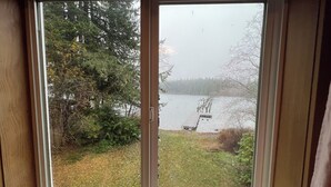 Uitzicht door een raam met houten kader, met een gazon, bomen en een waterpartij.