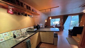 Een keuken met een spoelbak, kasten en een aanrecht. Er is een eethoek met een tafel en stoelen.