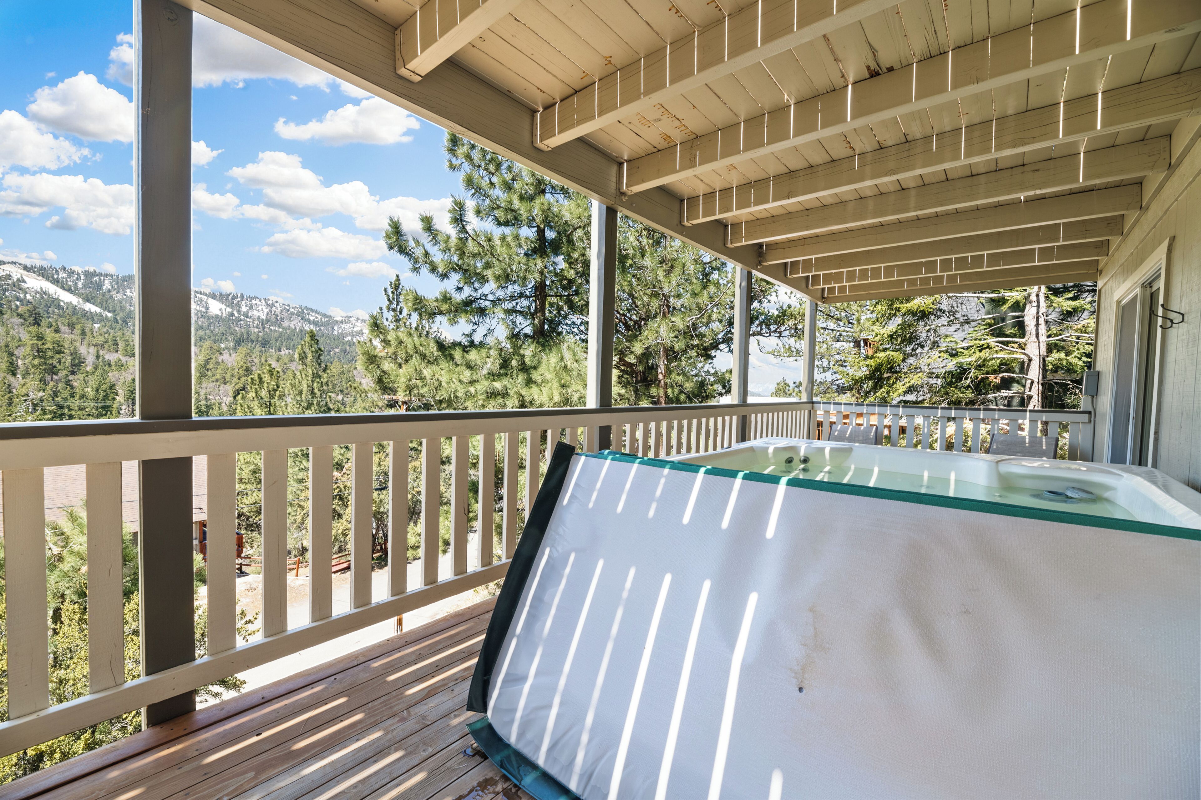 A covered outdoor area with a pool, wooden deck, and a view of a mountainous landscape.