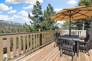 A wooden deck with a table and chairs, an umbrella, and a view of trees and mountains. - Paradise Pines (Big Bear Lake)