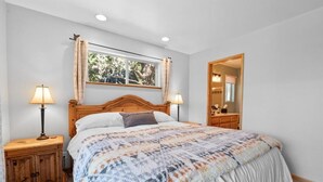 A bedroom with a wooden bed, two bedside lamps, a window with a view, and a mirror. - Paradise Pines (Big Bear Lake)