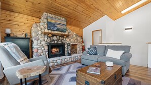 A cozy living room with a stone fireplace, a grey sofa, a wooden coffee table, and a rustic chair. - Paradise Pines (Big Bear Lake)