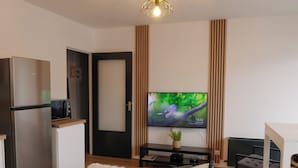 A modern living room with a flat-screen TV, a sofa, a dining table, and a kitchen area with a refrigerator and microwave. - Panoramik station +parking (Nancy)