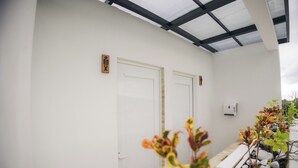 En korridor med hvide vægge, to døre, et lille område med planter og sten, samt et loft med en sort ramme.
