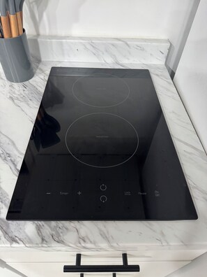 A black induction cooktop with a timer and lock function, placed on a marble countertop.