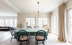 A dining room with a table set for four, a chandelier, and large windows with curtains.