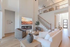 Ein geräumiges Wohnzimmer mit Kamin, großem Fernseher, einer Treppe und modernem Design.