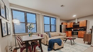 Ein Wohnzimmer mit Sofa, Couchtisch, Esstisch, Stühlen und einer Küchenzeile inklusive Schränken und Geräten.