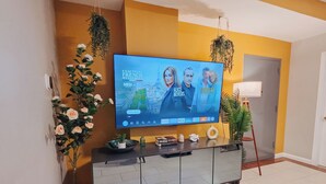 Ein Wohnzimmer mit Flachbildfernseher auf einer Kommode, einem Blumentopf und einem kleinen Tisch mit Dekoration.