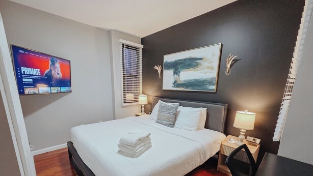 Ein Hotelzimmer mit Bett, Fernseher, Schreibtisch und einem Bild an der Wand.