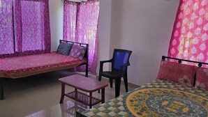 A room with a bed, a small table, a chair, and a round table with a patterned tablecloth. - Maa Durga Homestay (Guwahati)