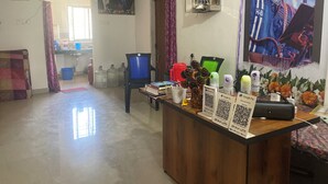 A room with a wooden reception desk, a blue chair, large water containers, a green chair, and a poster on the wall. - Maa Durga Homestay (Guwahati)