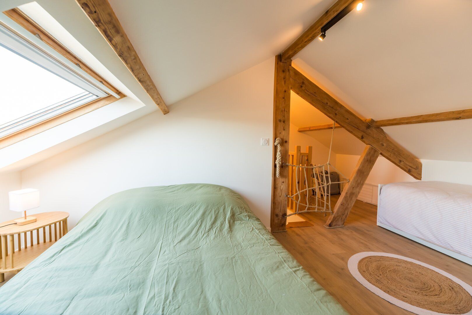 A loft bedroom with a sloped ceiling, a bed, a small table, and a rope swing.