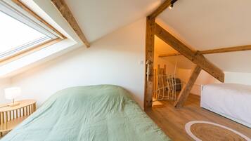 A loft bedroom with a sloped ceiling, a bed, a small table, and a rope swing.