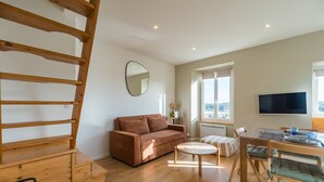 A living room with a sofa, a dining table, a TV, and a window with a view. - Renovated apartment with sea view - Trébeurden (Trébeurden)
