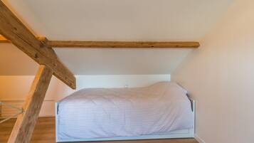 Quarto pequeno com cama de solteiro, teto inclinado e vigas de madeira aparentes.