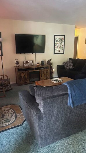 A living room with a large flat-screen TV, a wooden entertainment unit, a black sofa, and a patterned rug. - McCall Gem, Pet Friendly,  Fully Fenced, Fire Pit! (McCall)
