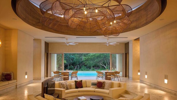 Un interior modern amb un sofà corbat, ventiladors de sostre i vista a una piscina.