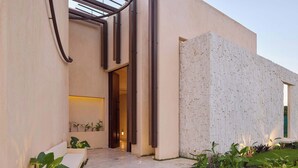 Edifici modern amb façana de formigó, entrada per una porta de vidre i una petita zona amb plantes.