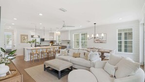Una sala moderna con un sofá grande, una zona de comedor y una cocina con armarios blancos.