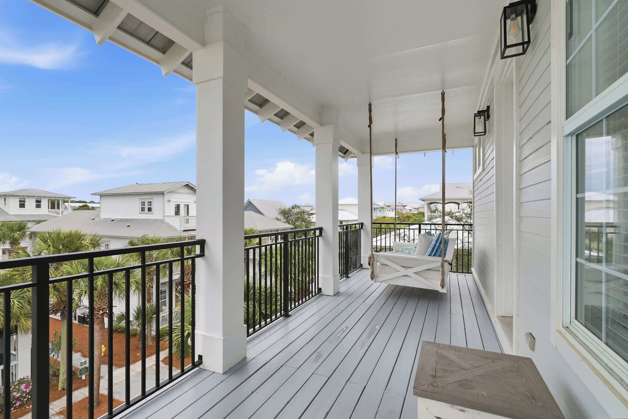 A covered porch with a swing chair, white railings, and a view of neighboring houses.