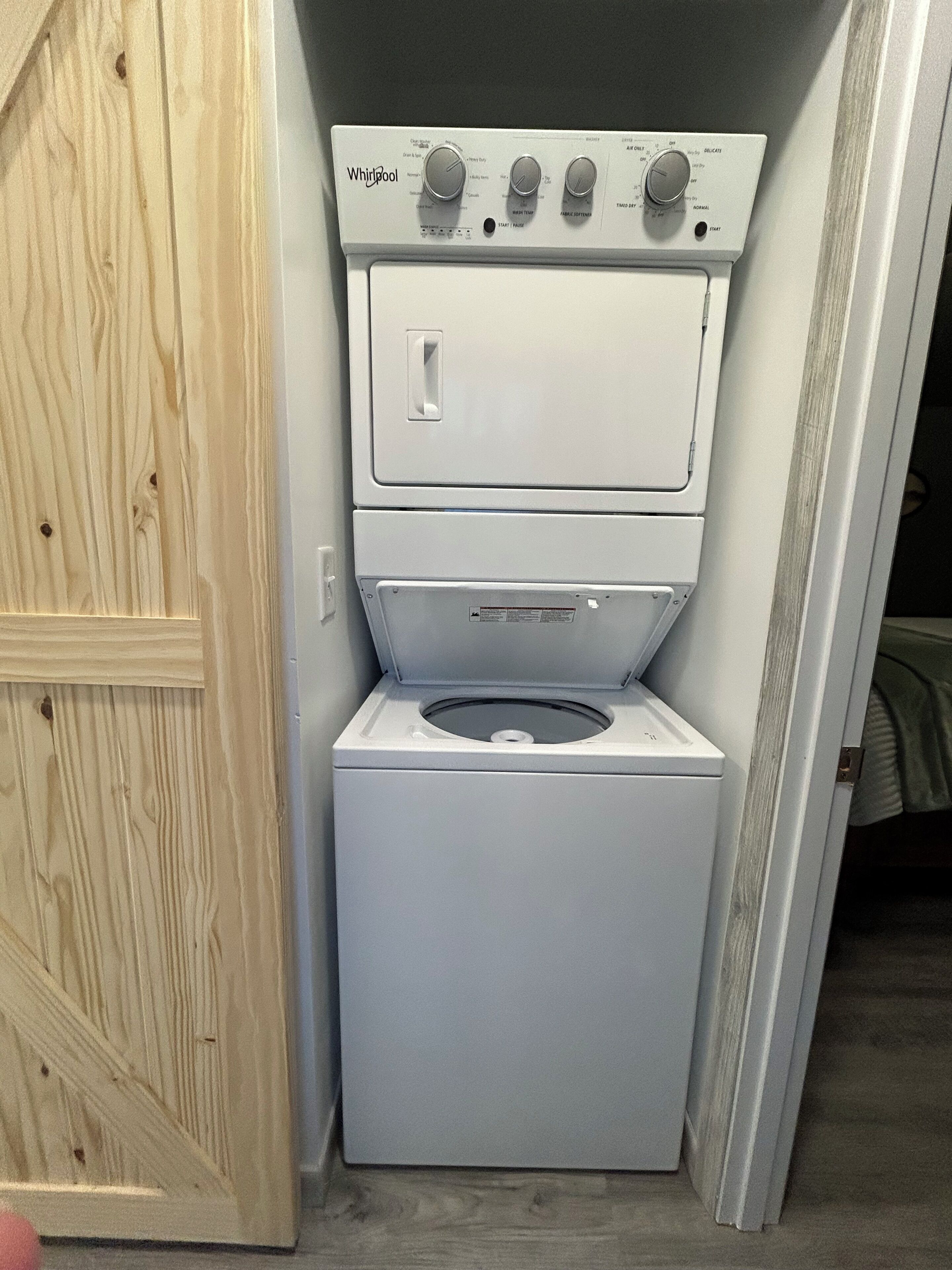 Eine kompakte Wasch- und Trocknerkombination in einem kleinen Waschraum mit Holztür und sichtbarem Schrank.