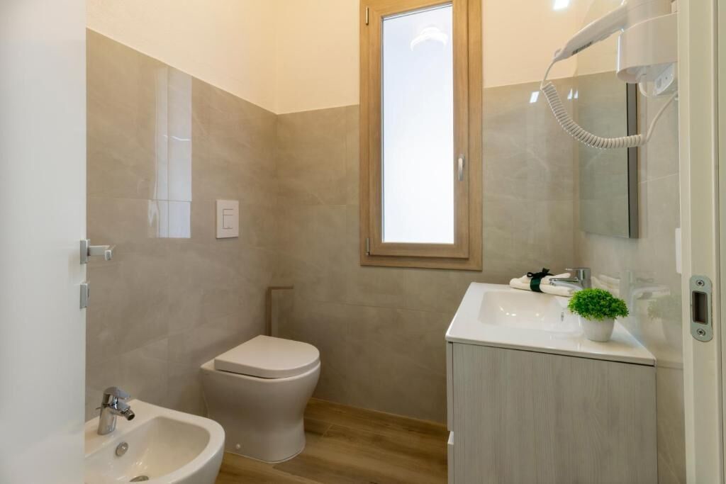 A bathroom with a toilet, bidet, sink, and a mirror with a hairdryer.
