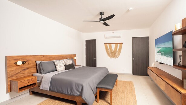 A modern bedroom with a bed, bedside tables, a ceiling fan, a TV, and a wall-mounted air conditioning unit. - The Pearl Jaco Beach (Jacó)
